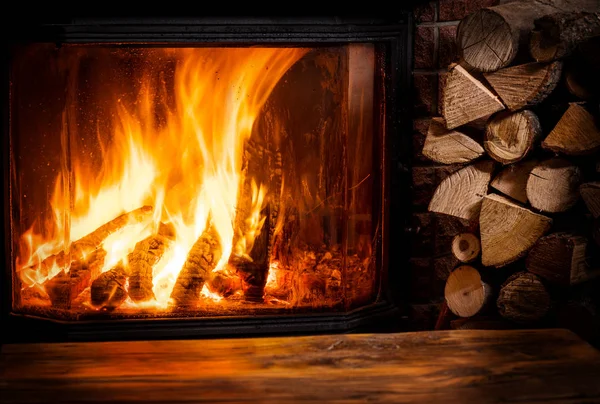 Gammalt träbord och öppen spis med varm eld i bakgrunden. — Stockfoto