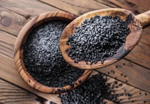 Black sesame seeds in the wooden spoon. Old wooden table and dis — Stock Photo, Image