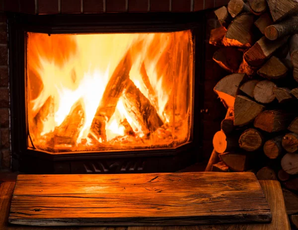 Leerer Holztisch und Kamin mit warmem Feuer im Hintergrund — Stockfoto