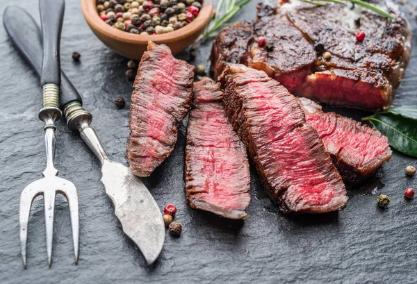 Středně vzácný steak z Ribeye s bylinkami na grafitové desce. — Stock fotografie