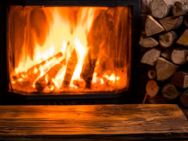 Oude houten tafel en open haard met warm vuur op de achtergrond. — Stockfoto