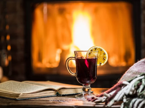 Hot mulled wine and a book on the wooden table. Fireplace with w — Stock Photo, Image