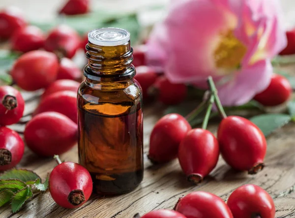 Rose-hips and rose hip seed oil on the wooden table. — Stock Photo, Image