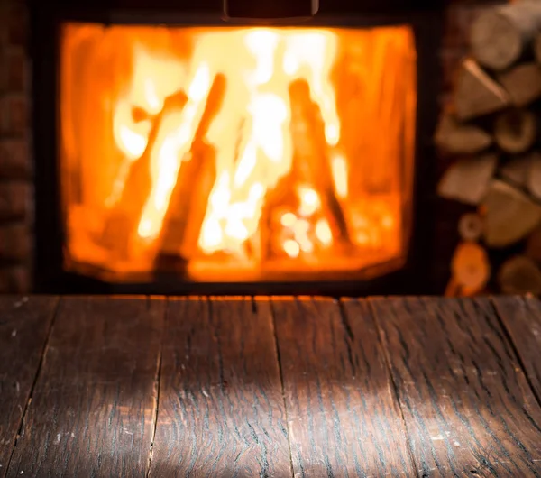 Empty wooden table and fireplace with warm fire at the backgroun — Stock Photo, Image