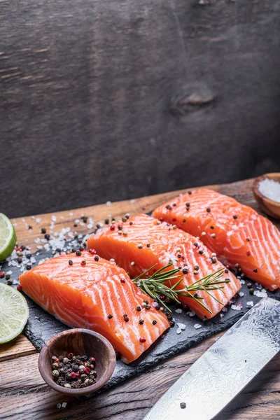 Fresh salmon fillets on black cutting board with herbs and spice — Stock Photo, Image