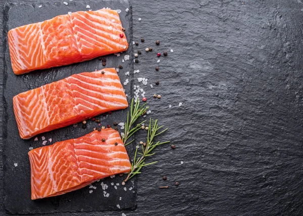 Otlar, baharatlar ile siyah kesme tahtası üzerinde taze somon fileto