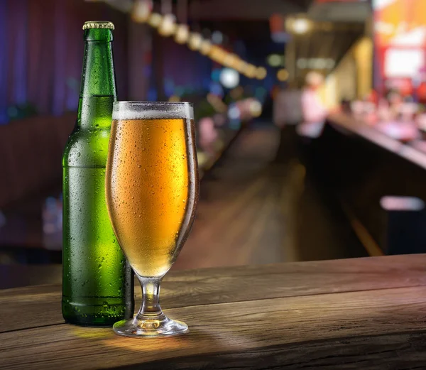バーカウンターの軽いビールとグリーンビールボトルのグラス. — ストック写真