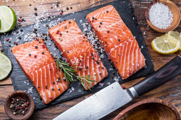 Fresh salmon fillets on black cutting board with herbs and spice — Stock Photo, Image