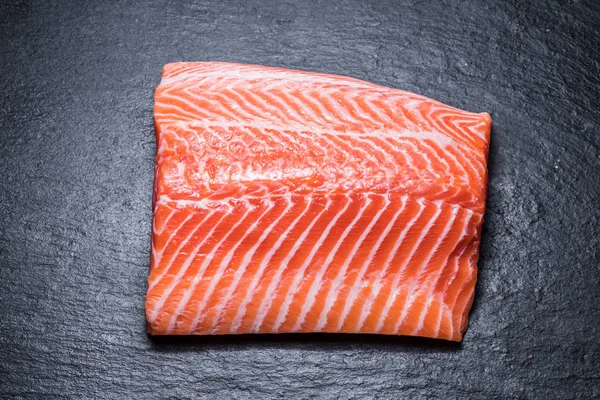 Filetto di salmone fresco sul tagliere nero . — Foto Stock