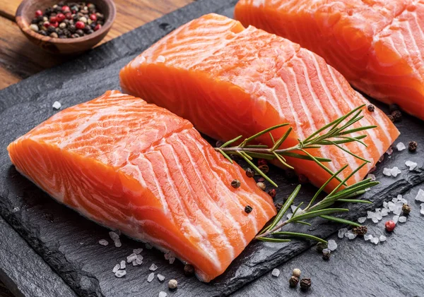 Filetes de salmón fresco en tabla de cortar negro con hierbas y especias —  Fotos de Stock