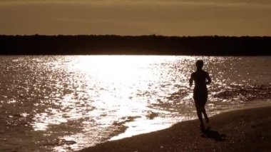 Kız batan güneşin altında okyanus sahillerinde koşuyor. Tek renkli sıcak arka plan ışıklandırması