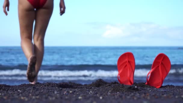 Kobieta Czerwonym Stroju Kąpielowym Kapeluszu Wchodzi Oceanu Czarnej Piaszczystej Plaży — Wideo stockowe