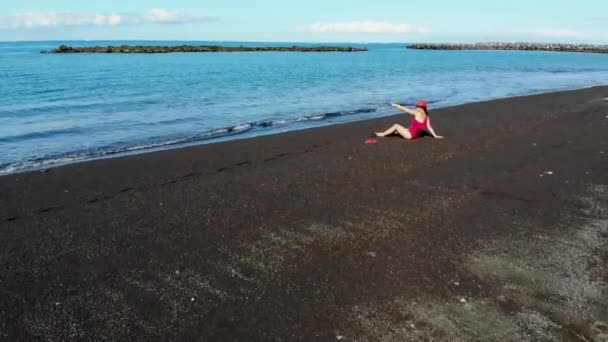 Kvinna Röd Baddräkt Och Hatt Sitter Svart Sandstrand Kanarieöarna Teneriffa — Stockvideo