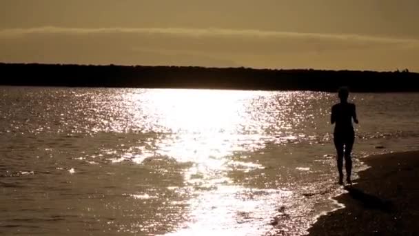 女孩在落日的余晖中沿着大海的海滩奔跑 单色暖光背光 — 图库视频影像