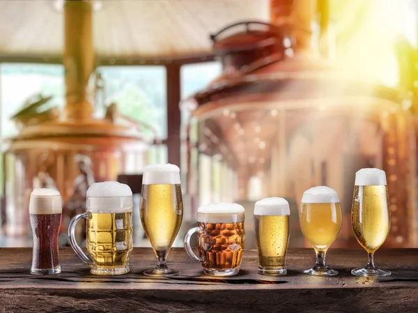 Pivní sklenice na dřevěném stole a měděný sud na vaření piva vzadu — Stock fotografie