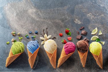 Gri arka planda meyve dilimleri olan waffle külahlı çeşitli renkli dondurmalar. Manzarayı aç.