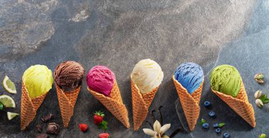 Gri arka planda meyve dilimleri olan waffle külahlı çeşitli renkli dondurmalar. Manzarayı aç.