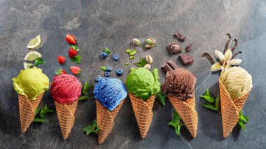 Gri arka planda meyve dilimleri olan waffle külahlı çeşitli renkli dondurmalar. Manzarayı aç.