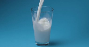 Süt mavi arka plandaki süt bardağına dökülür..