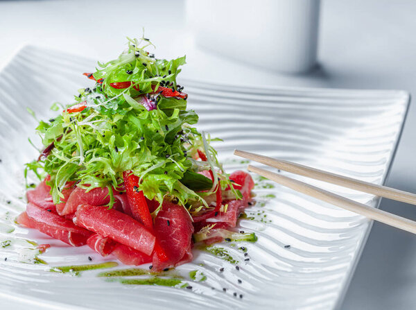 Элегантный салат с телячьим карпаччо в белой миске с палочками для еды.