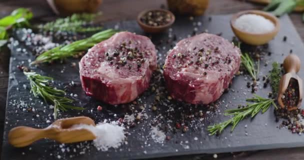Dva syrové žebírkové steaky s kořením a bylinkami na kamenném povrchu. Kamera se pomalu otáčí kolem steaků.