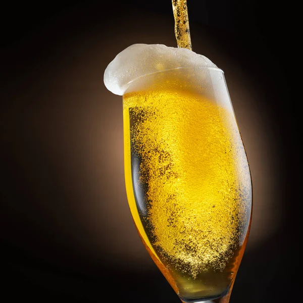 ビールのジェットがビールグラスに注ぎ込まれ 泡や泡がたくさん発生します 暗褐色の背景 — ストック写真