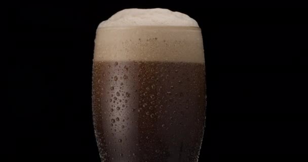 黒を基調とした黒ビールのグラス ガラス 泡および泡の上昇のビールの棒 ビールのガラスはゆっくりと時計回りに回転する — ストック動画
