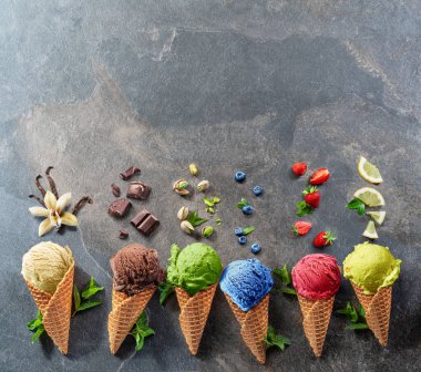 Gri arka planda meyve dilimleri olan waffle külahlı çeşitli renkli dondurmalar. Üst görünüm.