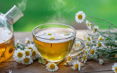 Eski ahşap masada bir bardak papatya çayı ve papatya çiçeği. Yakın plan..