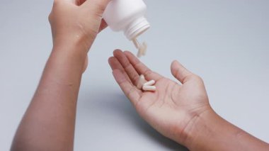 Beyaz kapsüller ya da plastik şişeden açık gri arka plana dökülen haplar. İlaç, sağlık, takviye ve ilaç tedavisi kavramı.