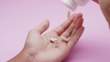Beyaz kapsüller ya da plastik bir şişeden pembe arka plana dökülen haplar. İlaç, sağlık, takviye ve ilaç tedavisi kavramı.
