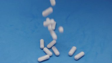 Beyaz kapsüller ya da plastik şişeden mavi arka plana dökülen haplar. İlaç, sağlık, takviye ve ilaç tedavisi kavramı.