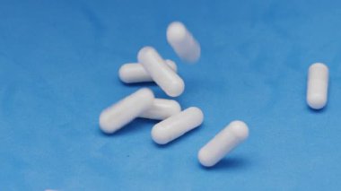 Beyaz kapsüller ya da plastik şişeden mavi arka plana dökülen haplar. İlaç, sağlık, takviye ve ilaç tedavisi kavramı.
