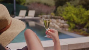 Bir yaz günü havuz kenarında bir bardak beyaz şarap içen bir kadın..