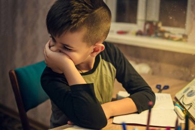 Okul ödevlerini yapıyor masada oturan genç çocuk