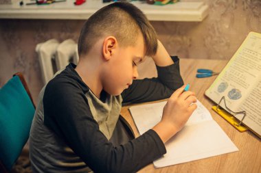 Okul ödevlerini yapıyor masada oturan genç çocuk