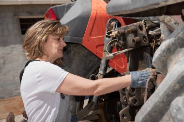 Kadın tamirci dışarıda traktör tamir ediyor.