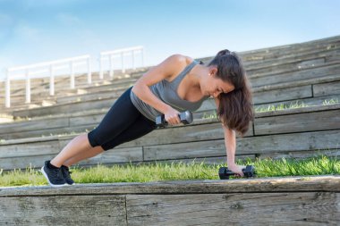 Ağırlıklarla egzersiz yapan bir kadın, dışarıda şınav çeken bir kadın.
