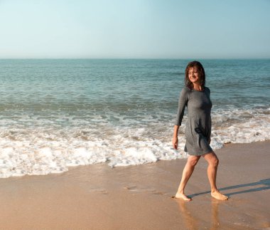 Sahilde yürüyen kadın geriye bakıyor.
