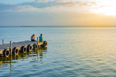 Bir iskelede, sırtüstü oturan bir çift
