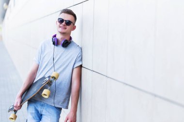 Modern bina Duvar tuğla önce gri t-shirt ve güneş gözlüğü giymiş kaykaycı longboard tutar