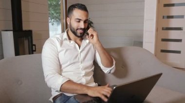 Tipik haftanın günü evden çalışan meşgul başarılı adam laptop, görevleri yerine getirmeye olarak Smartphone cep telefonu ile konuşmak