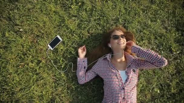 Дівчина слухає музику на траві — стокове відео