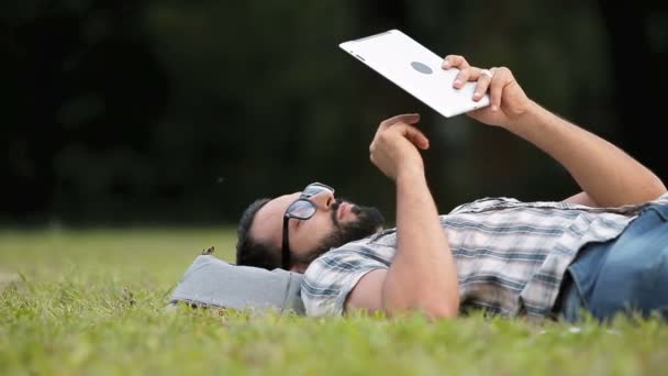 Man gebruikt Tablet liggen op gras — Stockvideo