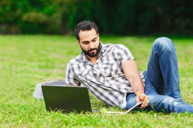 Sakallı öğrenci adam çimenlerin üzerinde rahatlatıcı