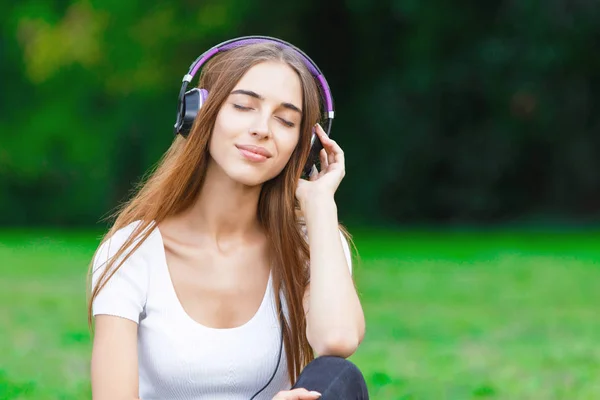 Jovem mulher em fones de ouvido no parque de verão — Fotografia de Stock