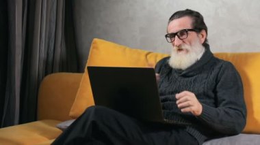 Konforlu, modern daire rahatlatıcı öğleden sonra harcama laptop yolu ile konuşmak hoş skype sahip neşeli yaşlı adam
