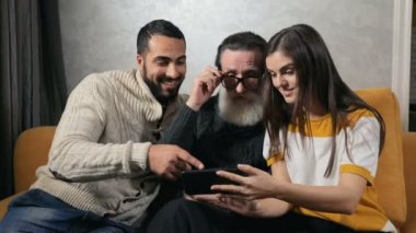 Yardımsever ve nazik torun smartphone, Büyükbaba sıcak aile ortamı, kapalı resimlerde tartışırken olarak eğlenmek için fotoğrafları gösterilen rahat sarı koltukta huzurlu akşam saat üzerinde ateş