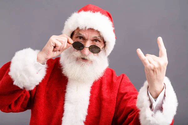 Papai Noel nos óculos de sol de pé e mostrando um gesto de rocha — Fotografia de Stock