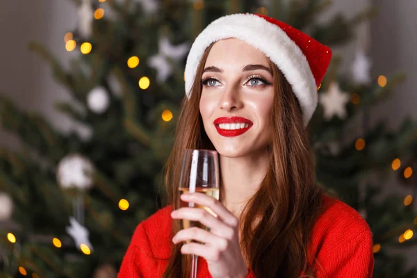 Hermosa mujer de Navidad con sombrero de Santa bebiendo champán mientras se hospeda cerca del abeto de año nuevo — Foto de Stock